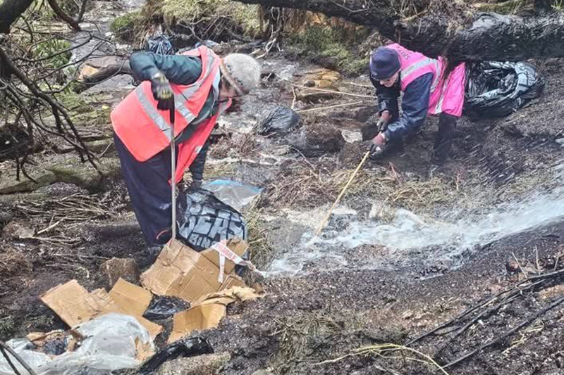 Two volunteers picking litter from a stream